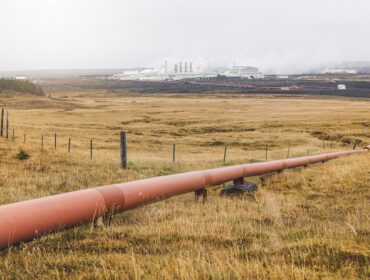 Geothermal Power Plant, hot water power station in Iceland. Steam rolling out of the plant chimneys, red large tubes running across the grounds filled with hot water. Sustainable, energy efficient Cloudy cold autumn day in Iceland.